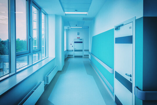 Daylight fills a corridor of a new hospital, where handrails support patients on the way to the wards. The frame is color graded in cool tones with added grain and a soft vignette