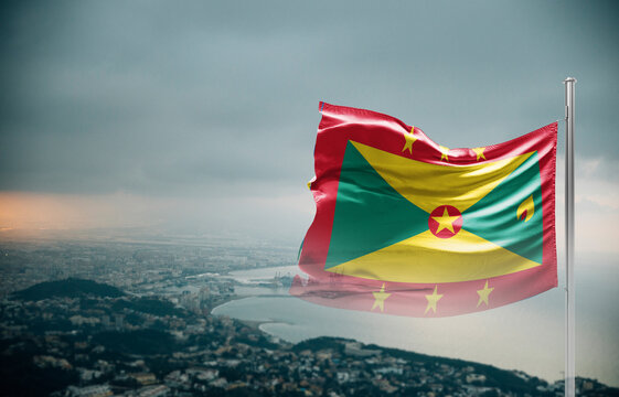 Grenada flag waving over a coastal city under dramatic cloudy sky, realistic fabric motion, aerial seaside landscape background. Grenada national flag for independence day.
