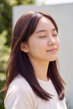 Outdoor sunlit closeup portrait of young woman with closed eyes and peaceful expression for wellness background and lifestyle design