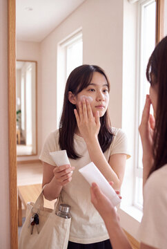 Woman applying facial cream in front of mirror with tote bag for morning skincare routine background and beauty care banner design