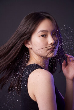 Young woman hair motion with glitter particles on dark background for beauty banner and cosmetic design
