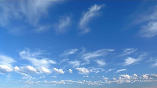 Time-lapse of wispy cirrus clouds drifting across a bright blue sky above a layer of cumulus clouds.