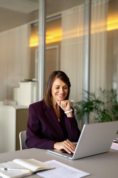 Latin businesswoman using laptop computer, thinking at office desk, vertical. 45 years old business woman works as consultant analyst advisor, joining web conference. Corporate lifestyle concept.