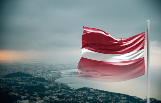 Latvia flag waving over a coastal city under dramatic cloudy sky, realistic fabric motion, aerial seaside landscape background. Latvia national flag for independence day.