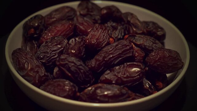 Dried medjool dates in white ceramic bowl, sweet organic date fruits on black background, traditional ramadan food and healthy snack