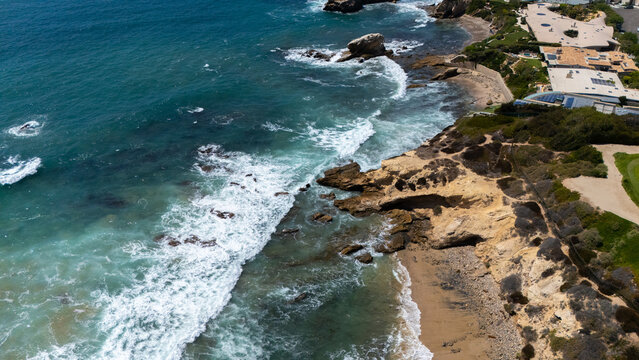 Aerial view of Crystal Cove with its rocky coastline, turquoise waves crashing against the shore, and coastal bluffs in Newport Beach, California, United States.