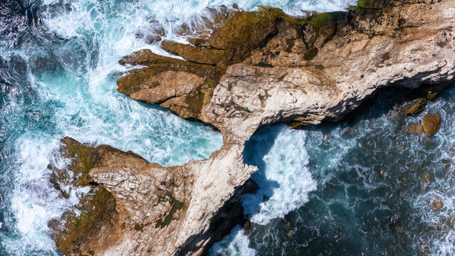 Aerial view of the rugged rock formations at Crystal Cove, with turquoise waves crashing against the cliffs and white sea foam in Newport Beach, California, United States.