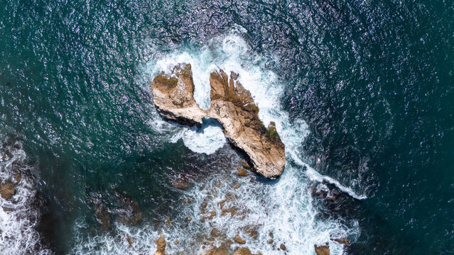Aerial view of Crystal Cove featuring rugged rock formations surrounded by crashing waves and deep blue ocean water in Newport Beach, California, United States.