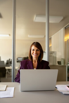 Confident businesswoman using laptop computer, typing at office desk, vertical. In 30s business woman works as consultant analyst advisor, reviewing sales figures, closing new deal. Success concept.