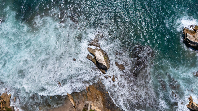Aerial view of Crystal Cove with turquoise ocean waves crashing against jagged rock formations and sandy shoreline in Newport Beach, California, United States.