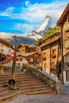 Zermatt, Switzerland iconic town street view in famous Swiss Alps ski resort, Matterhorn snow mount, bronze alphorn and houses