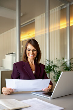 Elegant businesswoman reading document, reviewing paperwork at office desk, vertical. In 40s business woman works as executive banker leader, checking insurance form, accuracy driven. Career concept.