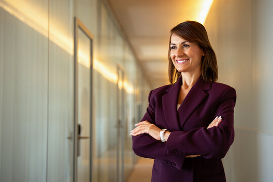 Cheerful businesswoman standing arms crossed in office corridor. 35 years old business woman works as executive banker leader, confident leadership pose, sophisticated appearance. Copy space.