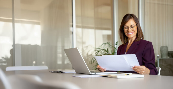 Confident businesswoman reading document, reviewing paperwork at office desk. In 30s business woman works as consultant analyst advisor, checking annual report, accuracy driven. Banner, copy space.