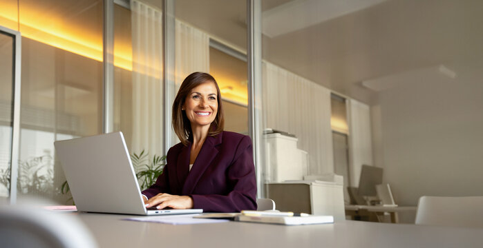 45 years old businesswoman using laptop computer, typing at office desk. Middle-aged business woman works as banker consultant advisor, updating sales database, closing new deal. Banner, copy space.