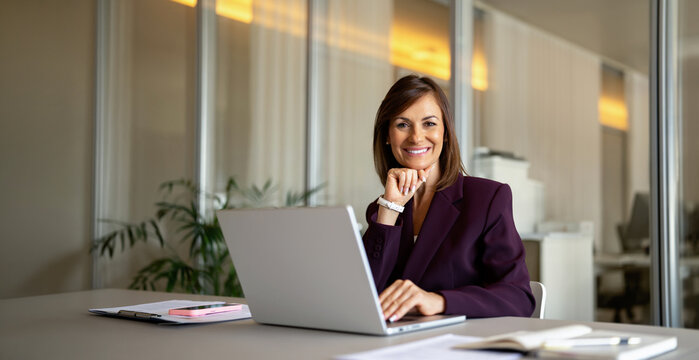 Mature businesswoman using laptop computer, thinking at office desk. Mid age business woman works as manager ceo executive, reviewing sales figures, forecasting quarterly budget. Banner, copy space.
