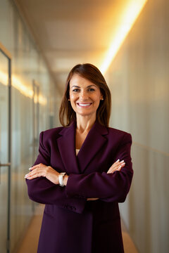 European smiling businesswoman standing arms crossed in office corridor, vertical. In 40s business woman works as consultant analyst advisor, confident leadership pose, polished style. Copy space.
