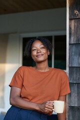 Obraz premium Relaxed woman leaning on a porch post with a mug wearing an orange tee casual lifestyle portrait for social media and advertising