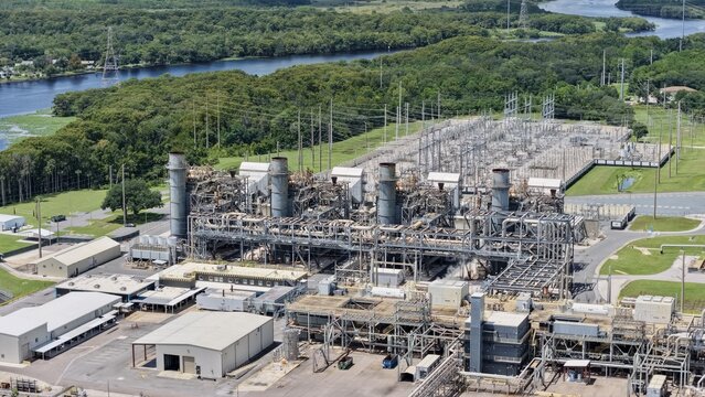 Aerial view of FPL Sanford Power Plant with its industrial structures, cooling towers, and electrical substation surrounded by lush greenery and a river in DeBary, Florida, United States.