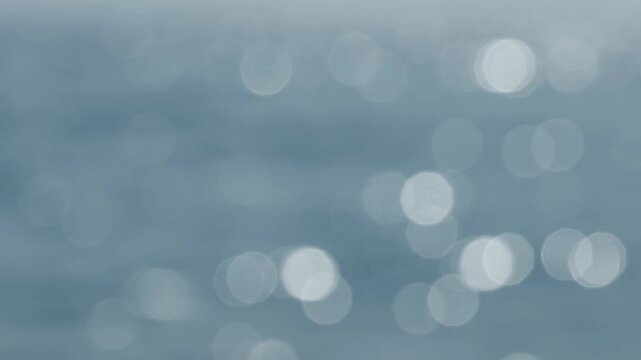 An out-of-focus blue sea surface with soft shimmering light reflections and abstract bokeh.