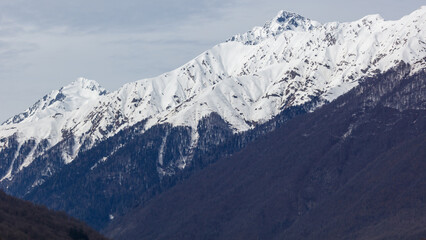 Fototapeta premium Alpine landscape features sharp, snow-dusted ridges and dark forested hillsides