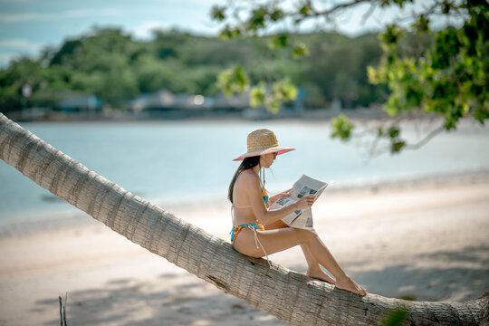 Woman tourist stay under shadow of the coconut trees at the edge of the sea beach, cheerfully traveling life in summer of the island