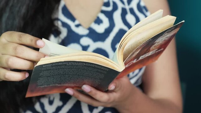 Close-up of a woman holding and reading an open book, representing reading, literature, learning, knowledge, relaxation, personal development and leisure.