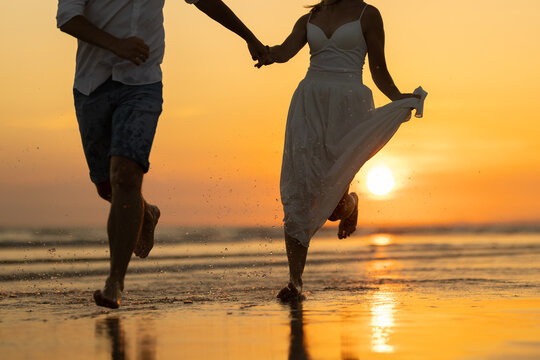 Couple walks hand in hand on the beach during sunset with waves and reflections in the sand