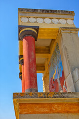 Naklejka premium A reconstructed section of the Palace of Knossos on Crete, Greece, featuring the characteristic red Minoan columns, decorated architectural elements and a colorful bull fresco.