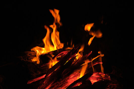 Glowing red-hot wooden logs with sparks and fading flames in a campfire.