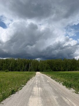 Gravel country road leading into dark storm clouds, dramatic rural landscape, travel and adventure, uncertainty and journey concept, approaching thunderstorm, lush green fields, moody sky, natural sce