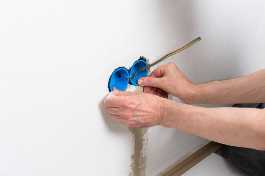 Skilled electrician carefully places blue flush-mount boxes into a wall opening, preparing for a new double electrical outlet installation in an apartment during home improvement