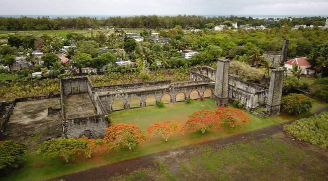 Aerial view of the historic Four a chaux lime kiln ruins featuring stone arches and chimneys surrounded by lush greenery and vibrant red flowering trees in Quatre Cocos, Flacq, Mauritius.