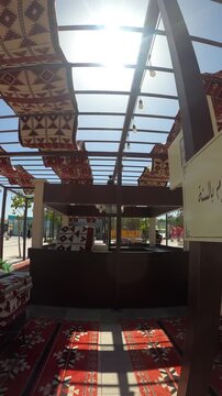 Sunlit outdoor Arabic seating area decorated with traditional red carpets.