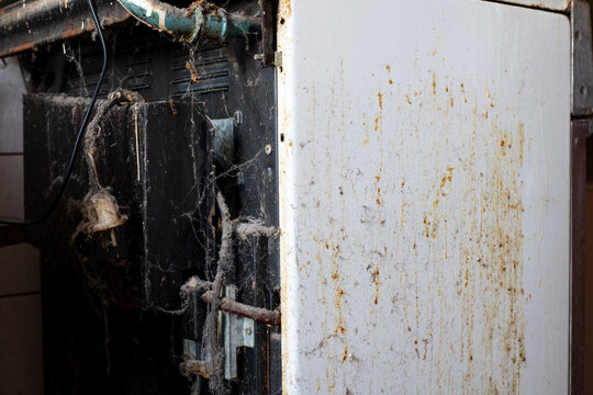 An old  gas stove, coated in soot and grease. This abandoned Soviet-era stove features a yellowed white enamel surface covered in soot, grease, and grime; exposed pipes and cobwebs are visible.