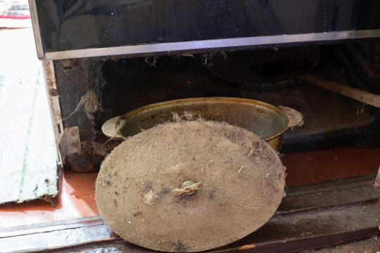 Dust and cobwebs surround a neglected pot resting beneath an old stove in a cluttered kitchen. This secret hideaway tells stories of meals long forgotten, echoing memories of the past.