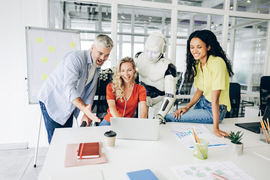 Diverse group of business team with robot collaborating on laptop working together at workplace