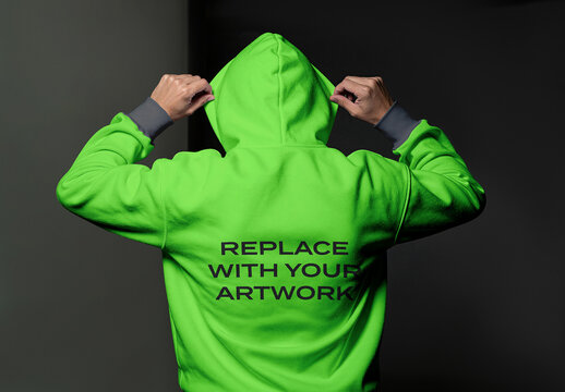 Back view of a person wearing hoodie with hands adjusting the hood, mockup template for artwork placement on clothing, studio environment dark background, indoor setting, casual apparel