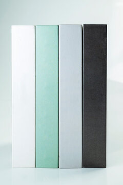 Four minimalist decorative books in white, mint green, grey, and black standing vertically on a clean white background. Study or education concept