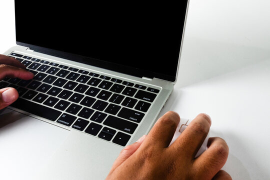 Close up of hands typing on a silver laptop keyboard and using a white mouse with a blank black screen. Concept of working from home, online business, coding, freelance, and internet surfing.