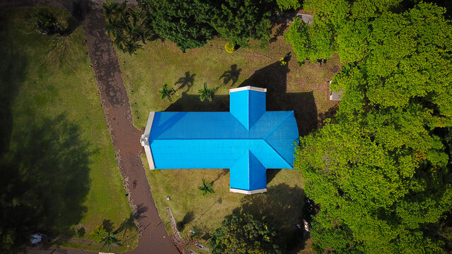 Aerial view of the bright blue roof of Chamarel Church surrounded by lush green trees and a dirt path in Chamarel, Riviere Noire District, Mauritius.
