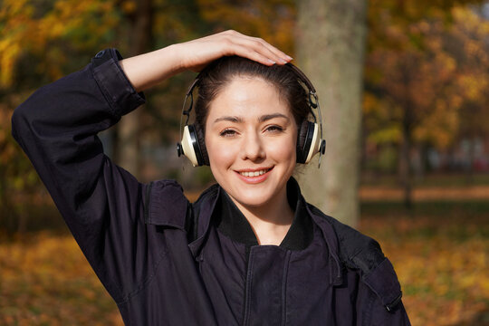 young woman shielding her head from the sun while enjoying autumn walk in a park with music from headphones