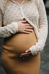 Obraz na płótnie Canvas A close-up photo of a young pregnant woman in a dress, gently holding her large belly in her hands. Waiting for a miracle. Pregnancy concept.