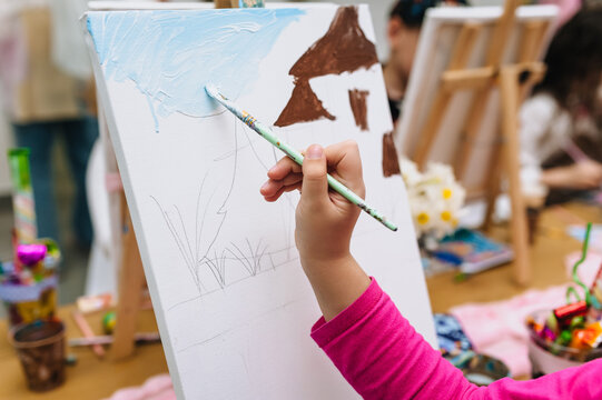 A photograph of a preschooler painting with a brush and watercolors on a white canvas or easel. Art concept.