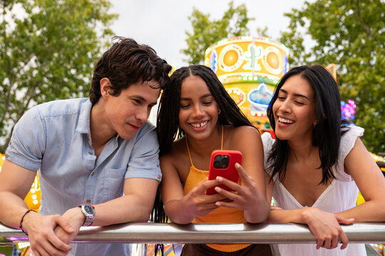 Group of diverse friends laughing while watching content on a smartphone at a fair