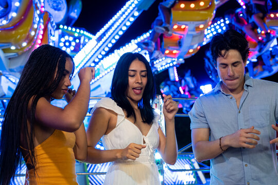 Friends dancing and celebrating together at a vibrant amusement park by night
