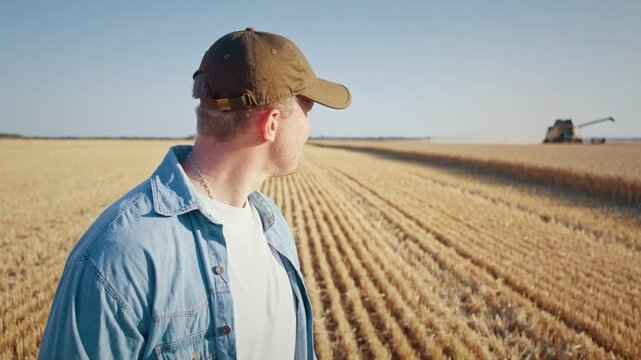Positive man farmer turns around to look at combine harvester