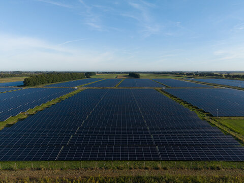 Aerial view of a vast solar farm with rows of photovoltaic panels installed in a rural field under a clear blue sky in The Netherlands.