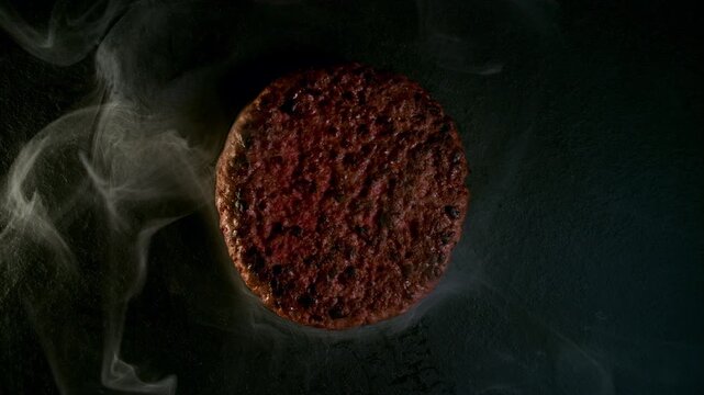 Top-down view of a juicy hamburger patty sizzling on a hot griddle, surrounded by aromatic smoke. Rich texture, golden browning and intense heat create a mouthwatering cinematic food scene.