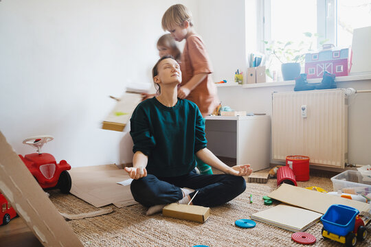 Stressed out mother sitting on floor while children running around her.